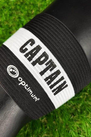 Black Optimum captain's armband with white CAPTAIN stripe wrapped around a black post on grass - Optimum