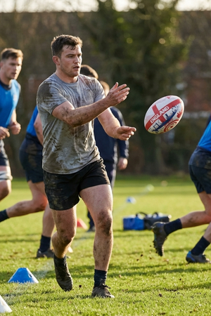 Muddy player passing a white and red Optimum England rugby ball in mid-air during training - Optimum