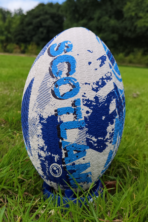 White and blue Optimum Scotland rugby ball upright on a kicking tee in grass with trees behind - Optimum
