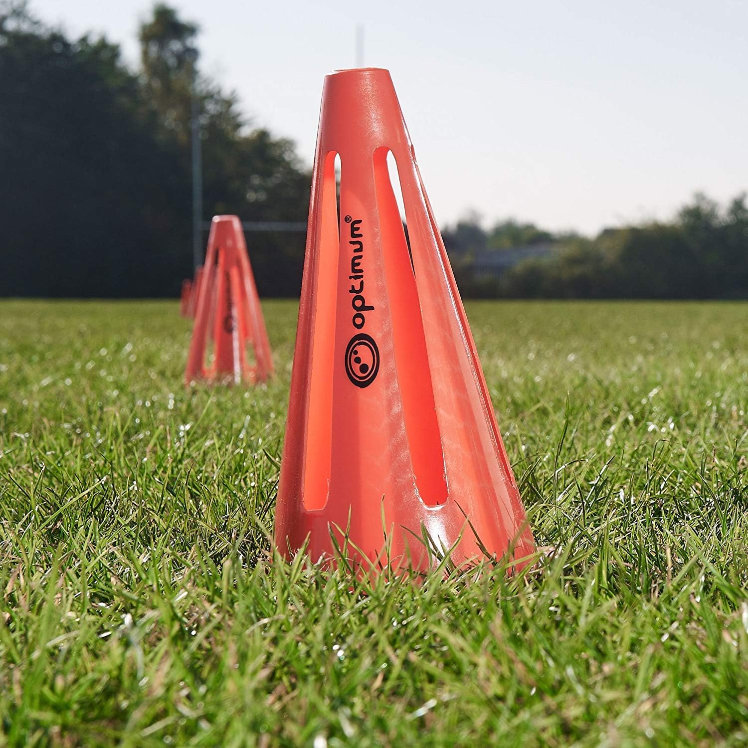 Red Optimum training marker cone with black logo standing on a grass pitch outdoors - Optimum