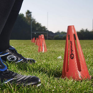 Red Optimum training marker cones lined up on grass beside a player's boots on a pitch - Optimum