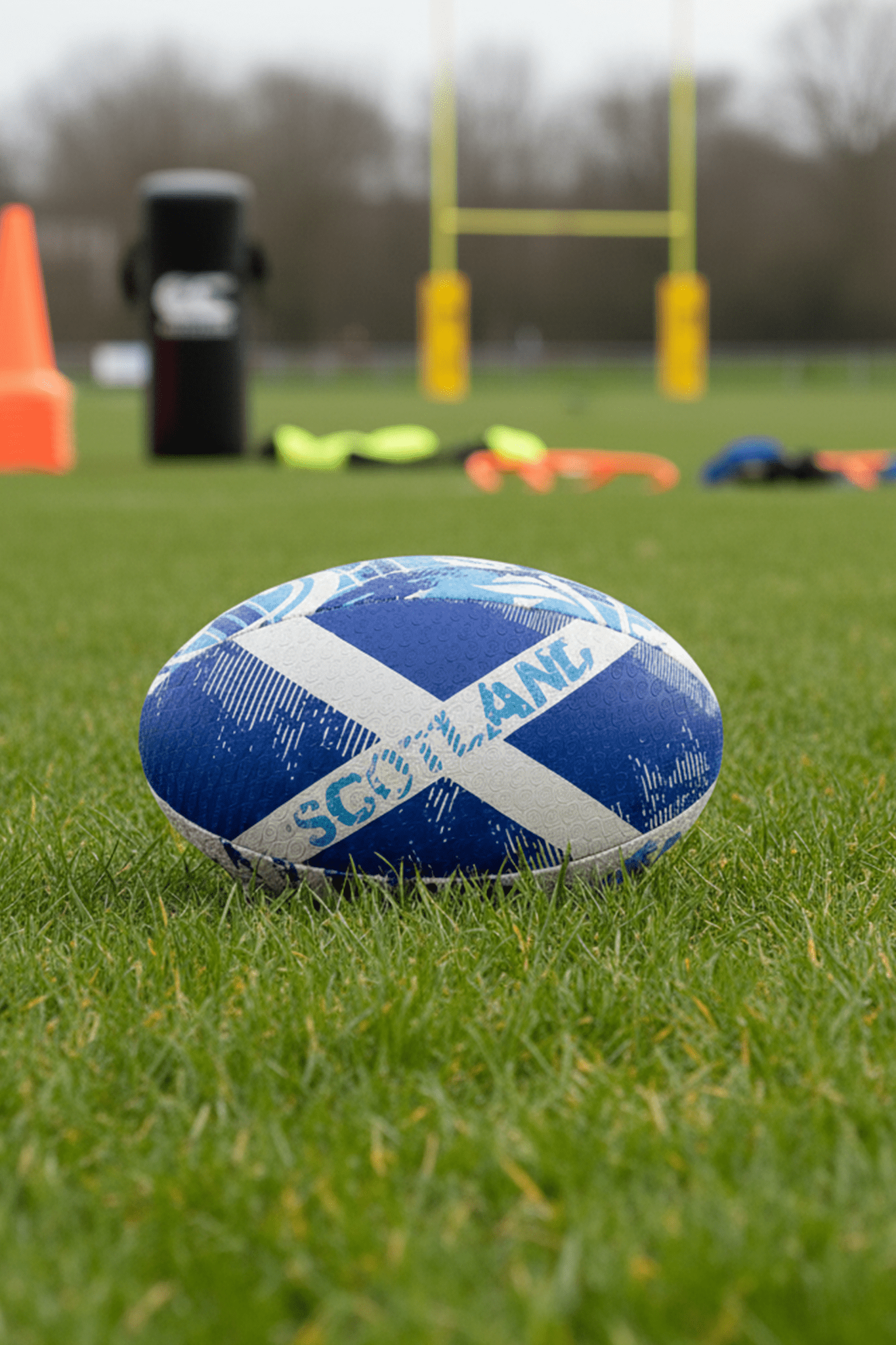 Blue Optimum Scotland rugby ball with white saltire and SCOTLAND print on grass by rugby posts - Optimum