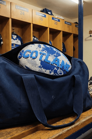 White and blue Optimum Scotland rugby ball in a navy kit bag on a changing-room bench - Optimum