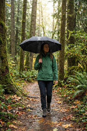 Woman holding open black Optimum compact umbrella on woodland trail in rain, lifestyle shot - Optimum