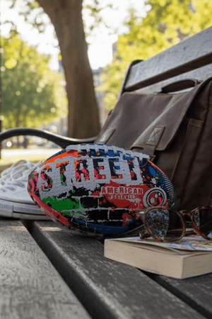 Multicolour Street American football on a park bench with satchel bag, sunglasses and book - Optimum