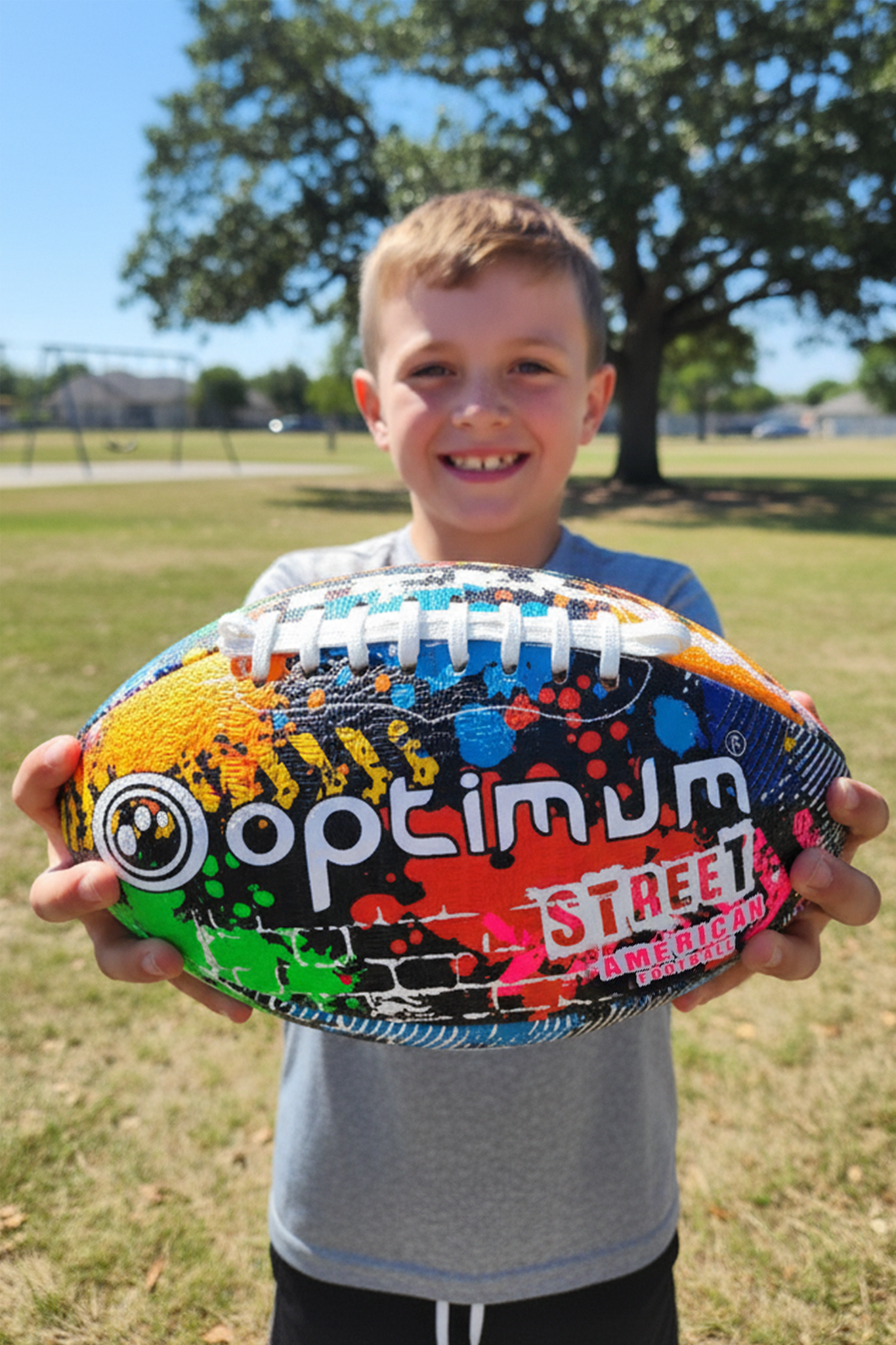 Boy holding out graffiti-print Optimum Street American football to camera, logo visible - Optimum