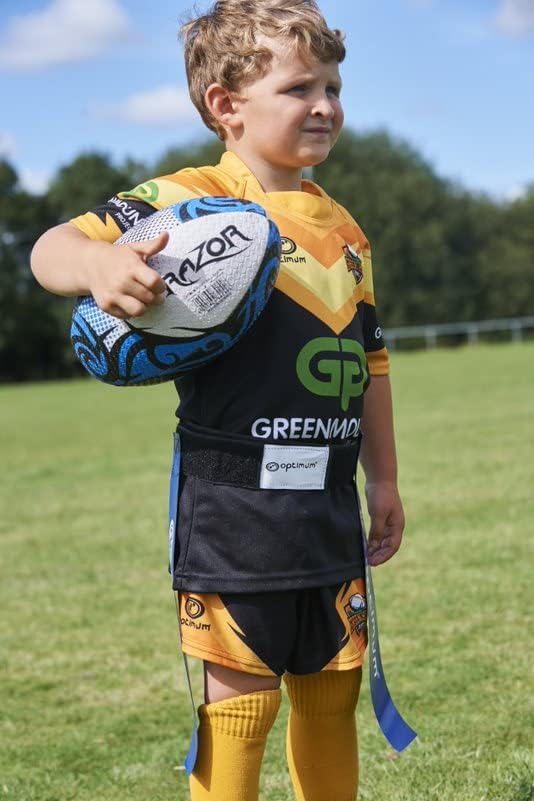 Young rugby player holding a ball wearing blue Optimum tag belt over orange and black kit, on grass