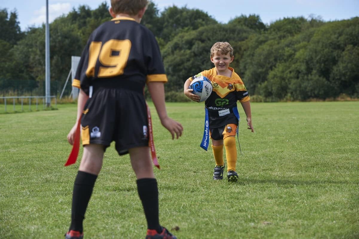 Young player running with ball in blue Optimum tag belt toward a defender in red flags, on grass