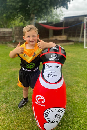 Young boy in rugby kit giving thumbs up beside a red Optimum inflatable tackle buddy in a garden - Optimum