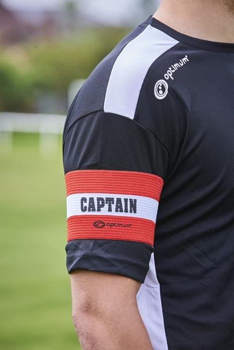 Red Optimum captain's armband with white CAPTAIN stripe worn on a player's arm over black kit - Optimum