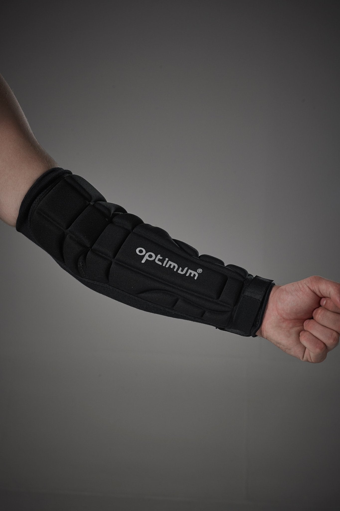 Arm wearing black Optimum padded elbow and forearm guard, grey studio background - Optimum