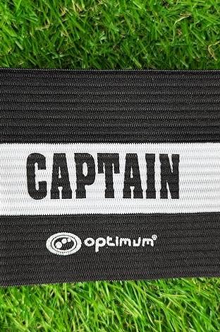 Black Optimum captain's armband with white CAPTAIN stripe and logo laid flat on grass - Optimum