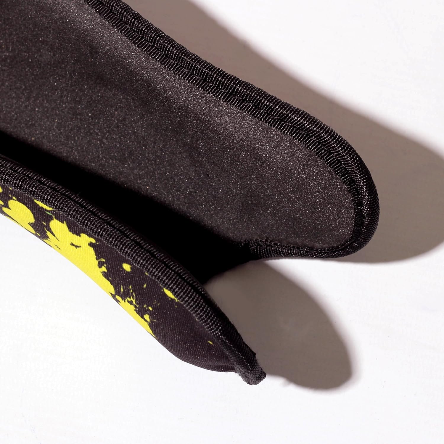 Close-up of black Optimum Fusion hockey shin guard padded reverse with yellow splatter edge, on white - Optimum