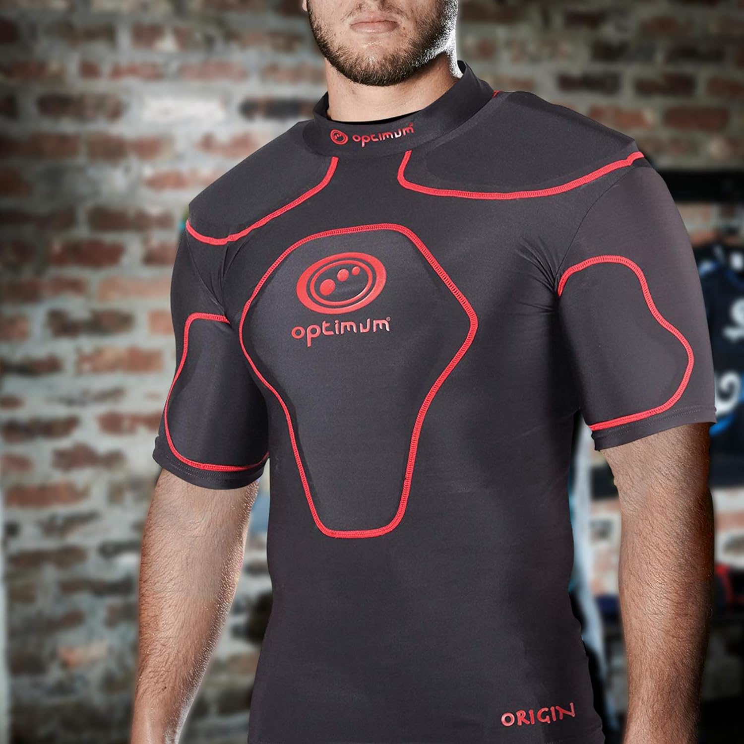 Man wearing black Optimum Origin rugby protective top with red trim and logo, brick wall setting - Optimum