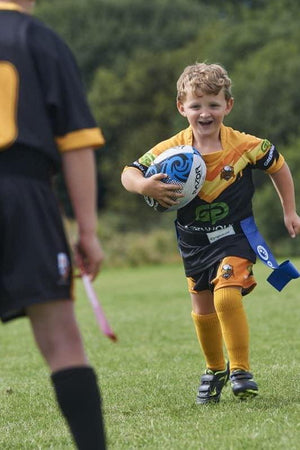 Young player running with ball in blue Optimum tag belt past a defender, on grass pitch