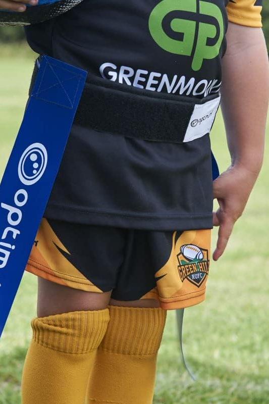 Blue Optimum tag rugby flag worn on a young player's waist over black and orange kit, on grass