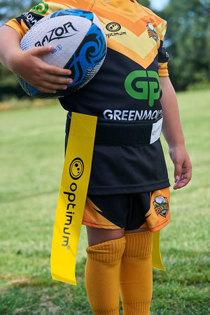 Yellow Optimum tag rugby flag worn on a young player's waist holding a ball, on grass pitch