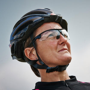 Cyclist in black helmet wearing Optimum sunglasses with clear lenses against grey sky, lifestyle shot - Optimum